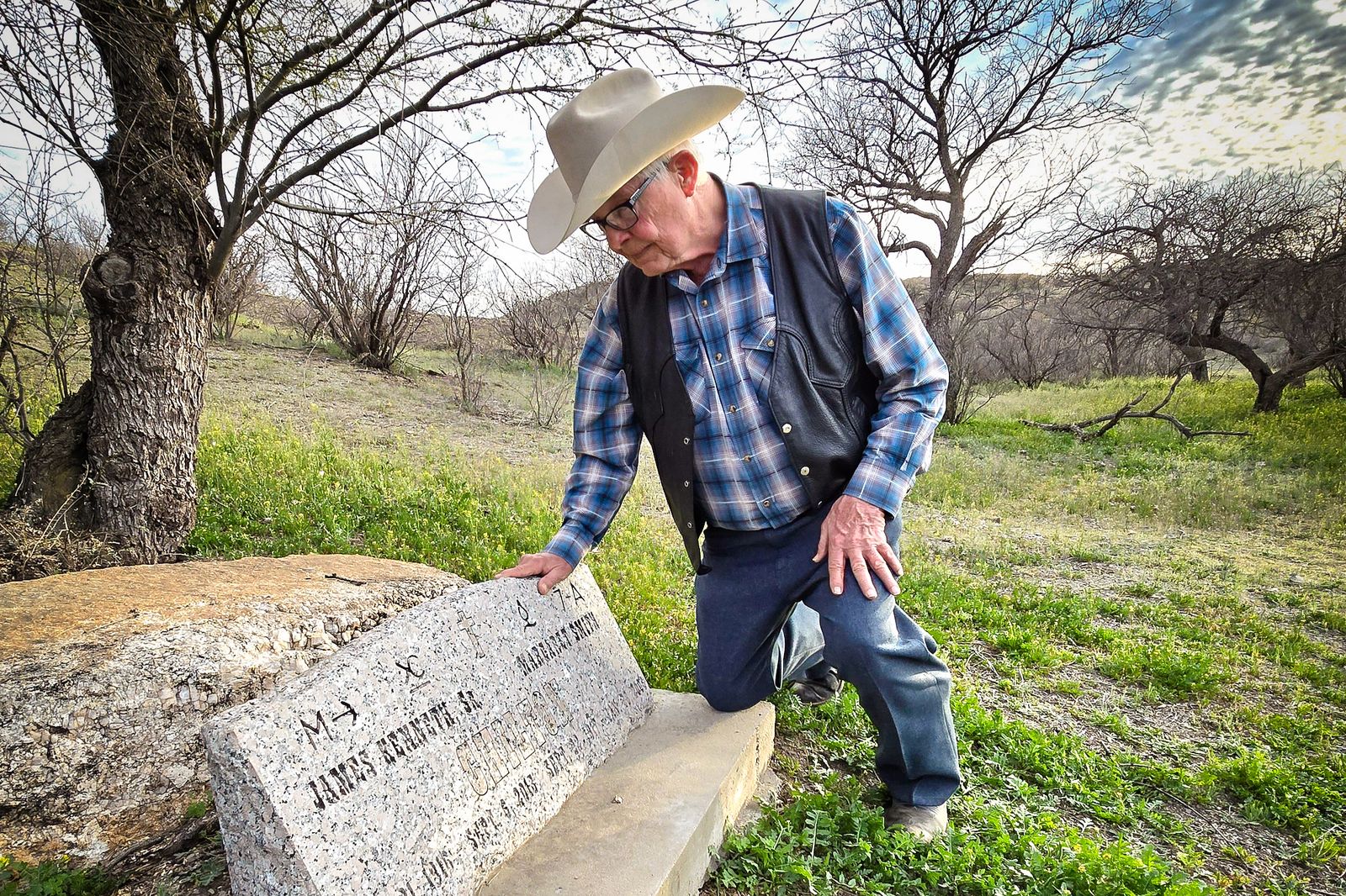 Ông Jim Chilton quỳ gối trước khu đất của gia đình trong khuôn viên trang trại nơi cha mẹ ông được chôn cất, hôm 22/03/2024. (Ảnh: Allan Stein/The Epoch Times)