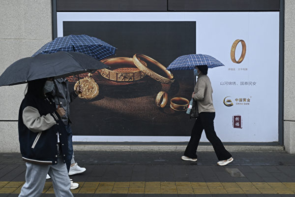 Một khách bộ hành đi ngang qua tấm biển quảng cáo vàng ở Bắc Kinh, hôm 10/04/2024. (Ảnh: Wang Zhao/AFP)