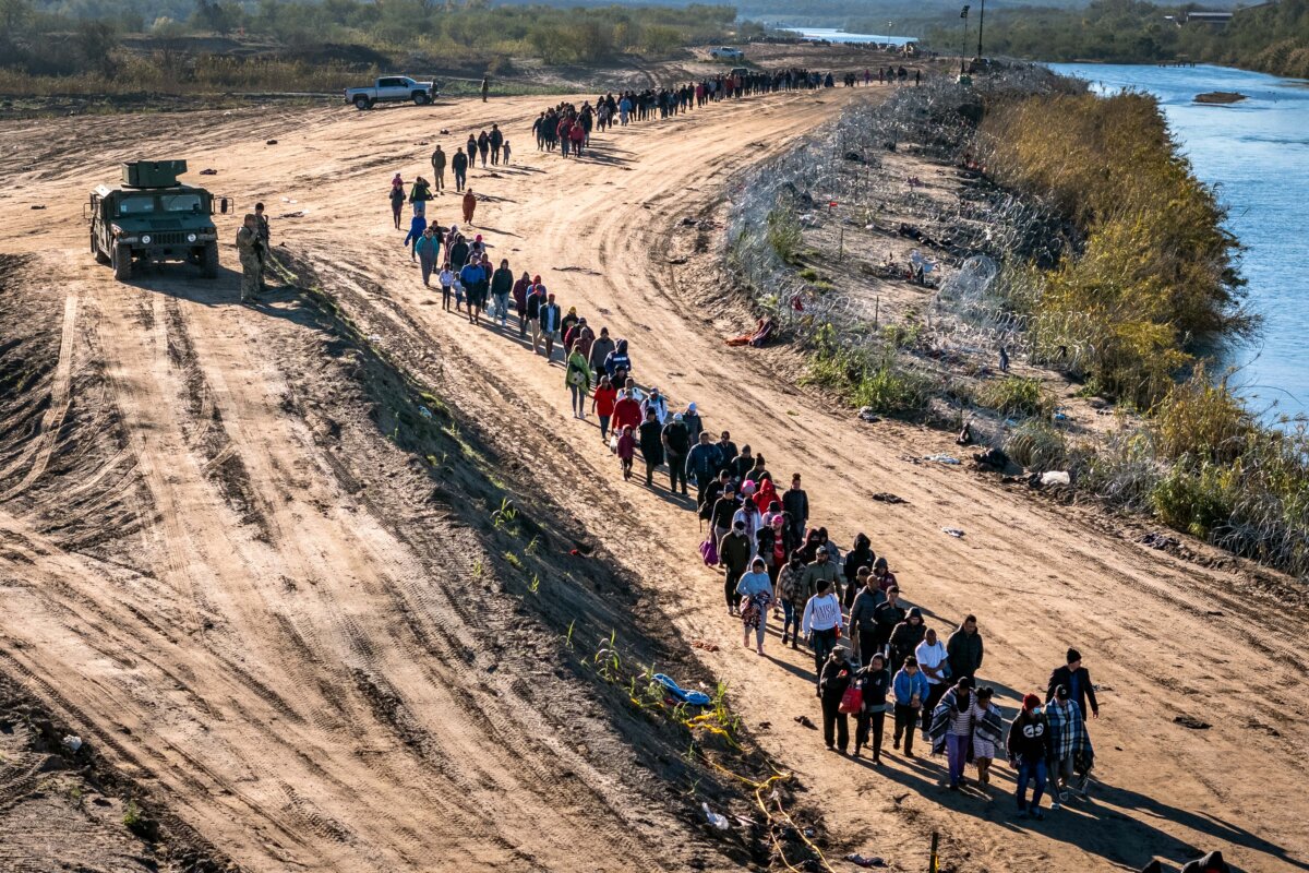 Một đoàn hơn 1,000 người nhập cư bất hợp pháp đi về phía trung tâm giải quyết thủ tục tại hiện trường của lực lượng Tuần tra Biên giới Hoa Kỳ sau khi họ vượt sông Rio Grande từ Mexico ở Eagle Pass, Texas, vào ngày 18/12/2023. (Ảnh: John Moore/Getty Images)