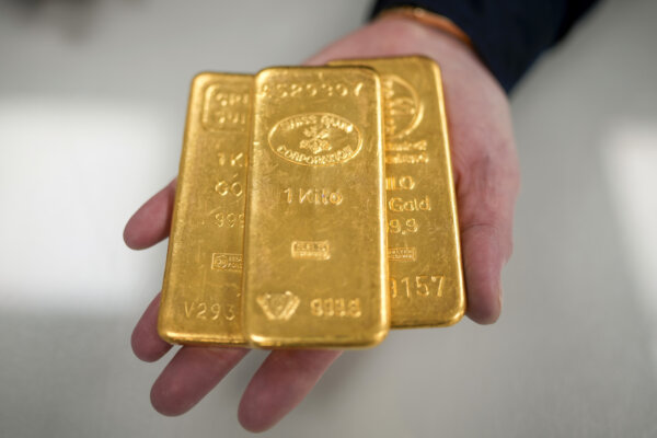 Một nhà giao dịch vàng nguyên chất chụp ảnh với ba thỏi vàng nặng 1 kg ở Birmingham, Anh, ngày 13/12/2023. (Ảnh: Christopher Furlong/Getty Images)
